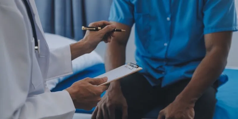 Doctor with clipboard talking to patient on exam table.