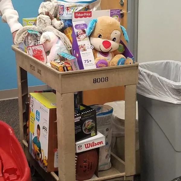 A cart with toys sits by a trash can.