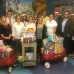 People indoors smiling and posing with wagons of toys.