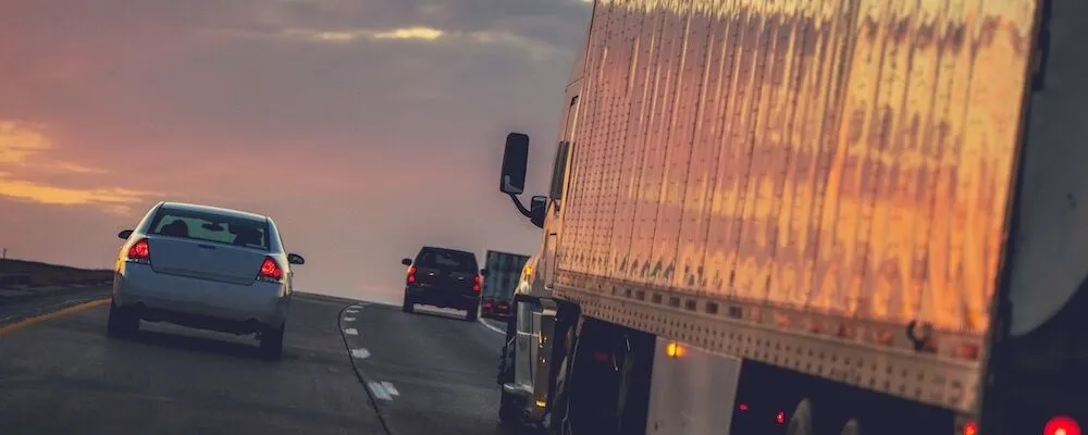 A white car, black SUV, and truck drive at sunset.