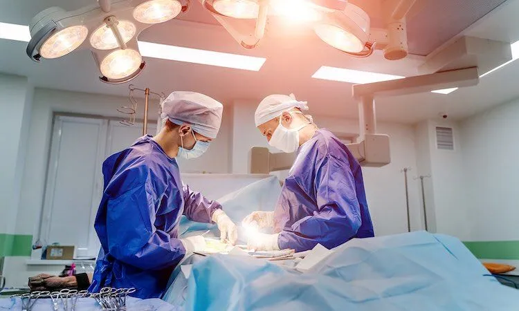 Two surgeons perform surgery under bright operating room lights.