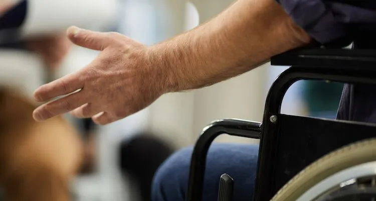 Hand resting beside wheelchair as person gestures thoughtfully.