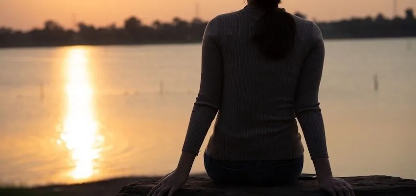 A person with long hair sits on a rock.
