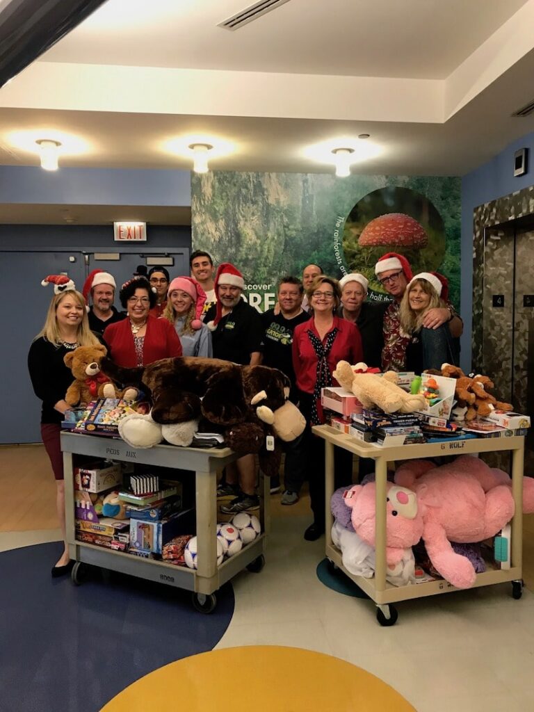People in Santa hats smile behind carts of toys.