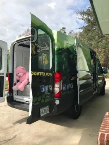 Green van with back doors open shows pink teddy bear.