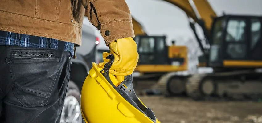 Person in gloves and jacket holds a yellow hard hat.